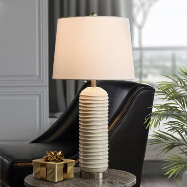 White porcelain table lamp with small gift wrapped in gold next to it.