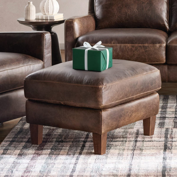 Brown leather ottoman with green gift on top of it
